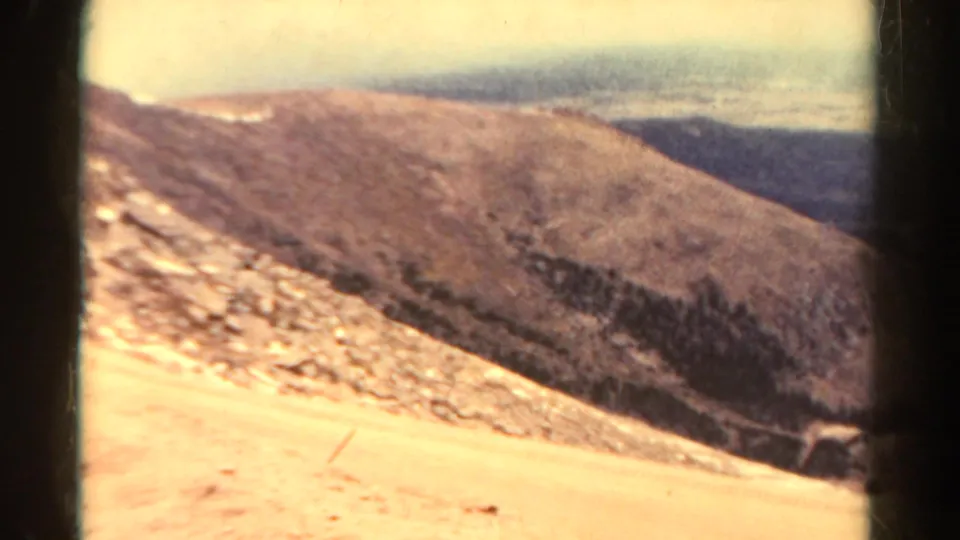 A 1967 Colorado mountain landscape view shows sunlit rocky slopes, distant ridges, and a hazy sky.