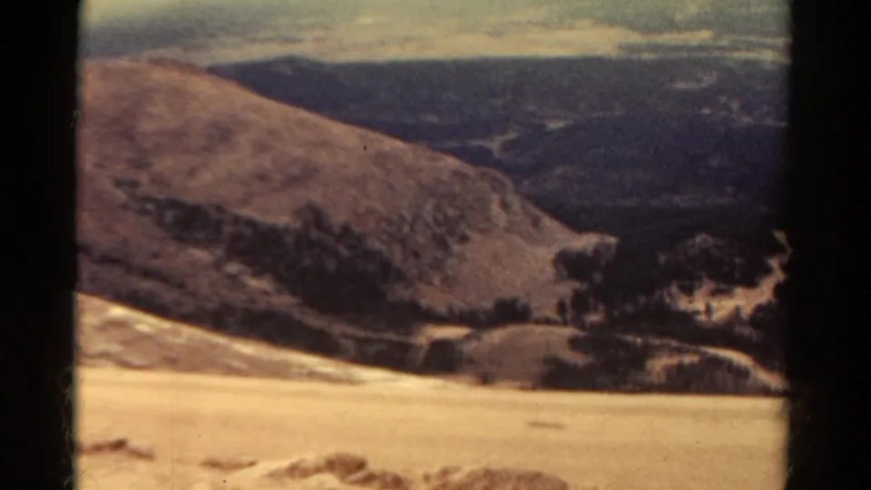 A 1967 Colorado landscape frame shows a broad rocky slope, valley shadows, distant hills, and soft 8mm color.