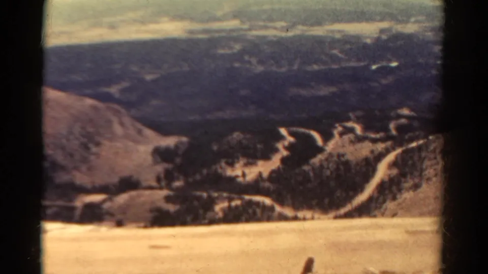 1967 Colorado 8mm frame of a mountain and high-desert overlook, with pale hillside foreground and winding roads below.
