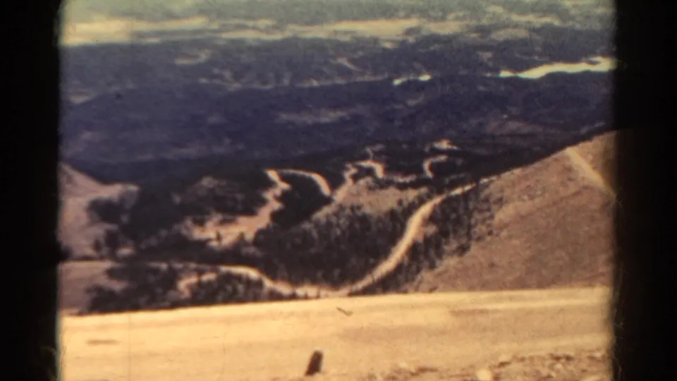 1967 Colorado 8mm frame emphasizing winding road lines, dark ridges, and a pale high slope in a broad landscape view.