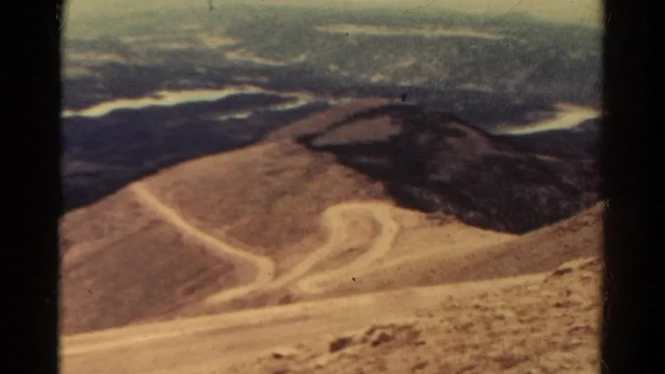 1967 Colorado 8mm frame showing a winding dirt road across arid mountain terrain, with dark brush and distant ridges beyond.