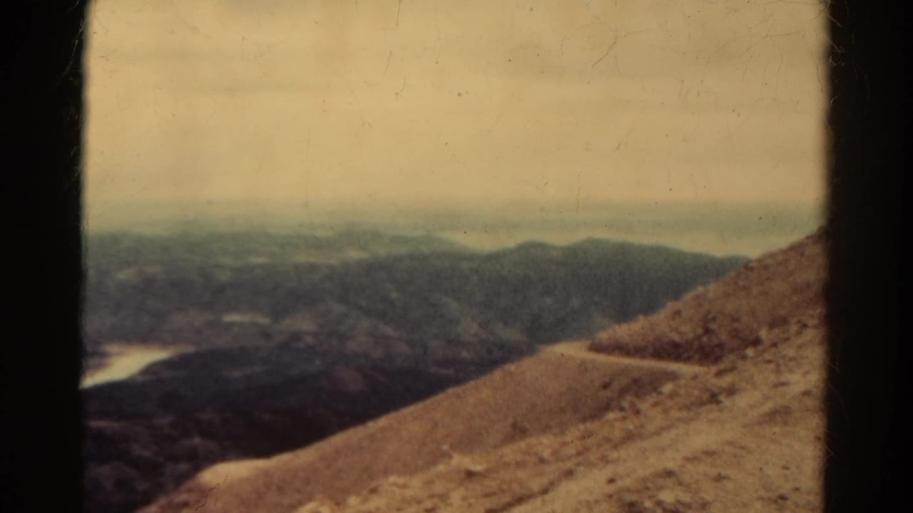 Rocky slope edge with a narrow winding trail and hazy mountains in the distance.