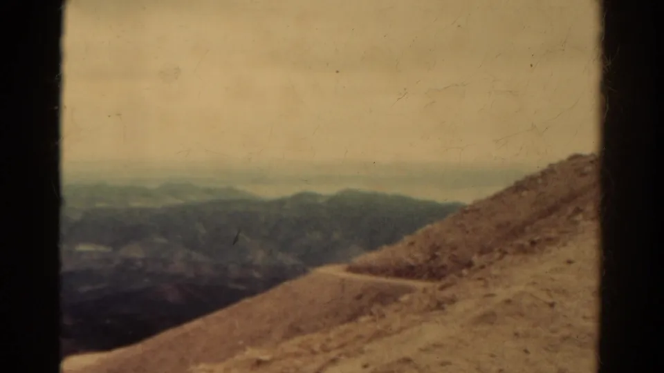 Faded 8mm Colorado view of a barren hillside trail with shadowed ridges and a soft cloudy horizon.
