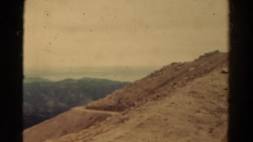 1967 8mm Colorado frame showing a dirt path crossing an arid mountain slope toward hazy distant ranges.