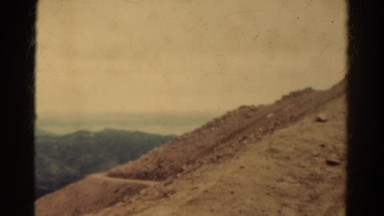 1967 Colorado 8mm frame showing a rocky slope, winding dirt path, distant hills, hazy sky, and visible film borders.