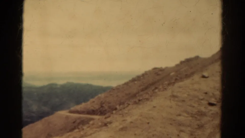 1967 Colorado 8mm frame showing a rocky slope, winding dirt path, distant hills, hazy sky, and visible film borders.