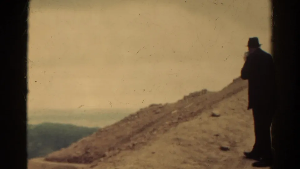 1967 Colorado home-movie frame with the man partly at right, facing a rocky slope and distant hazy hills.