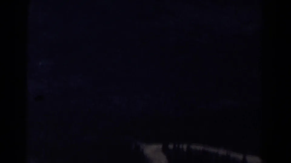 1967 Colorado 8mm frame with a dim, blue-toned mountainside view, heavy gate-edge darkness, and a pale ridge or road line near the bottom.
