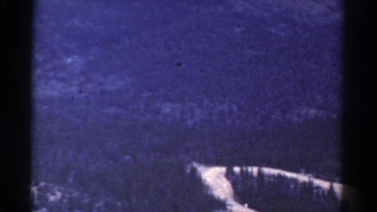 Blue mountain slope with grain and a pale diagonal ridge or road near the lower right.