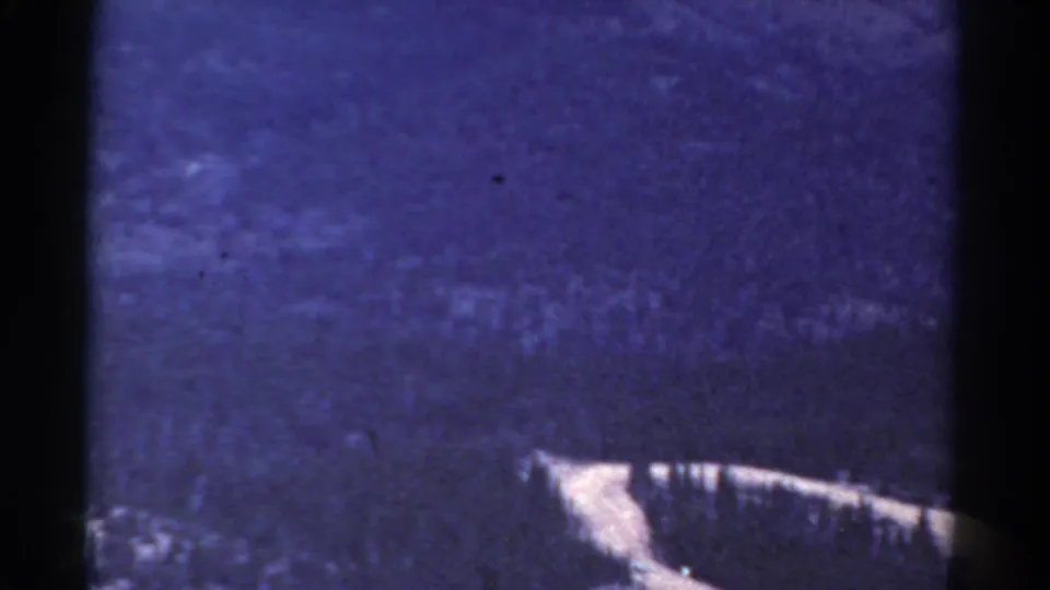 1967 Colorado home-movie frame showing a hazy blue mountainside with visible grain and a pale diagonal feature near the lower edge.