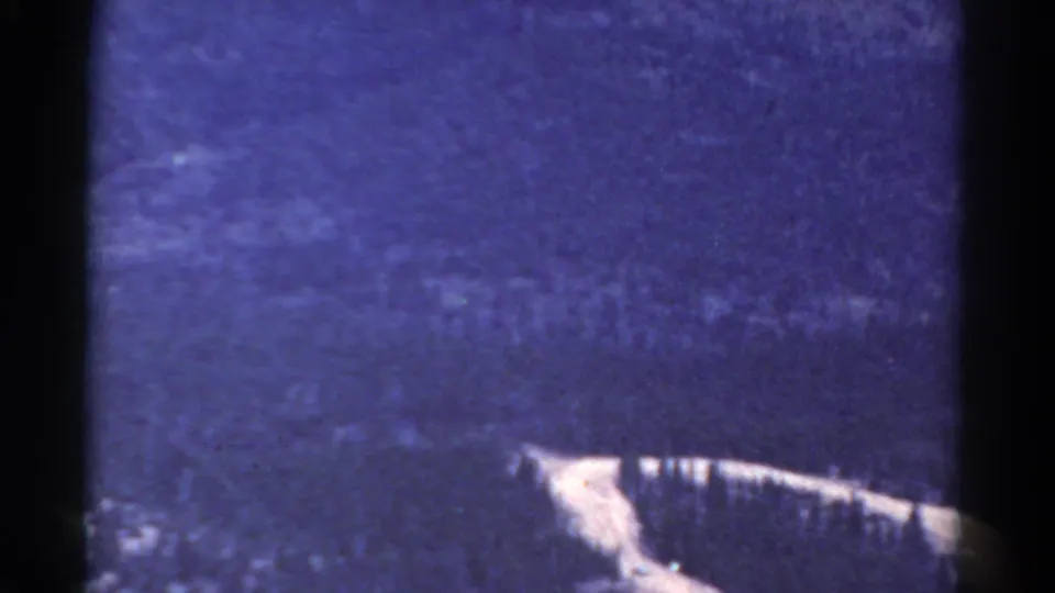 1967 Colorado 8mm frame with a hazy mountainside, dense grain, dark vertical border, and a pale ridge or road-like line along the lower edge.