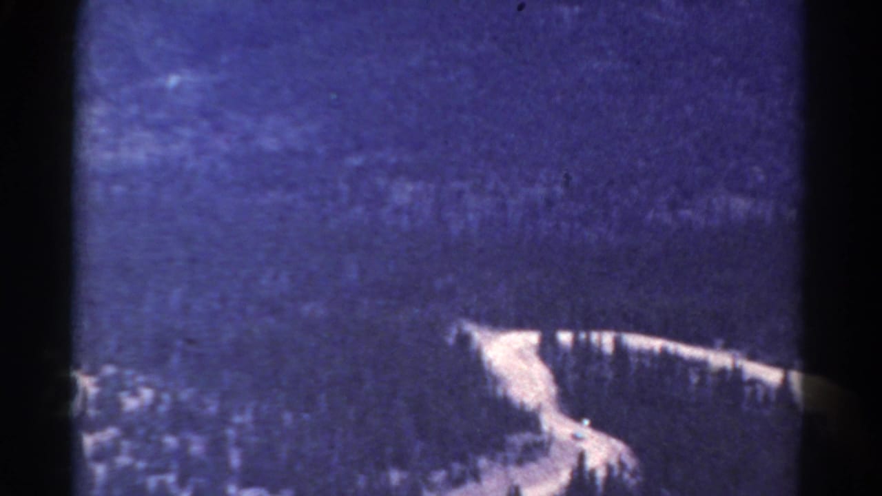 1967 Colorado 8mm frame showing a light river curve through dark forested mountains, with visible grain and edge shadowing.
