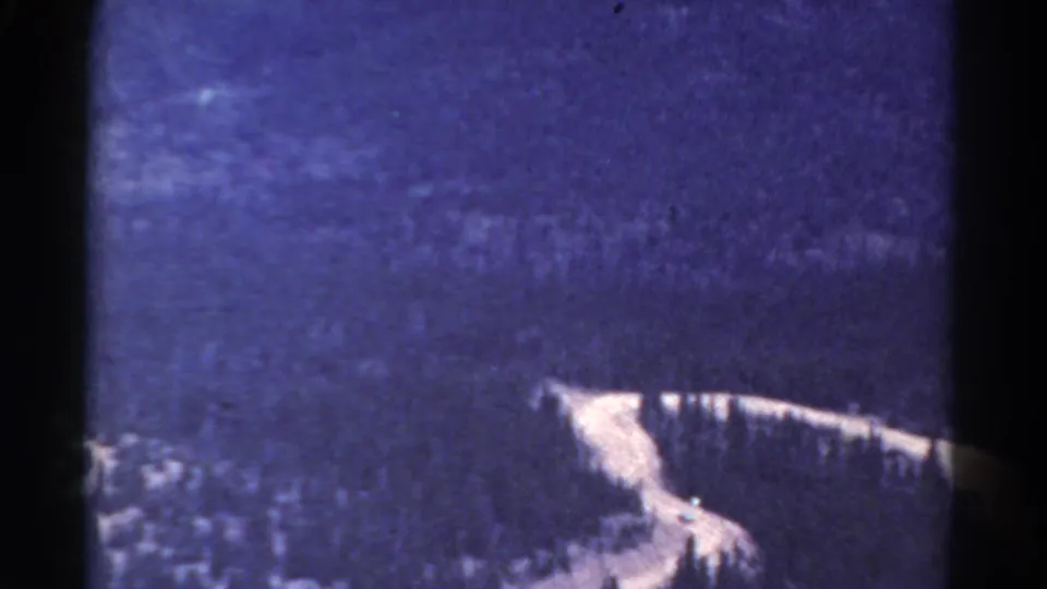 1967 Colorado 8mm frame showing a light river curve through dark forested mountains, with visible grain and edge shadowing.