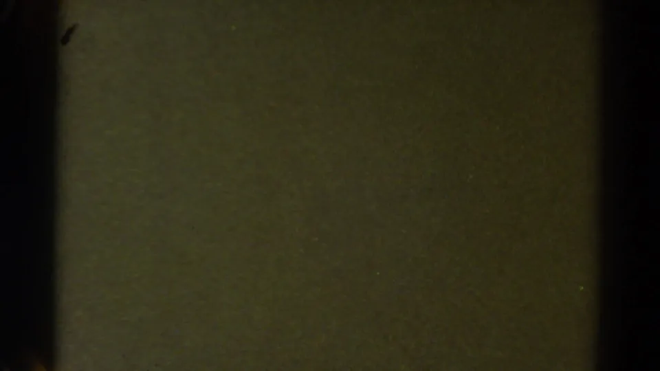 Underexposed 8mm frame from the 1967 Colorado clip, showing mostly dark terrain color and visible film texture.