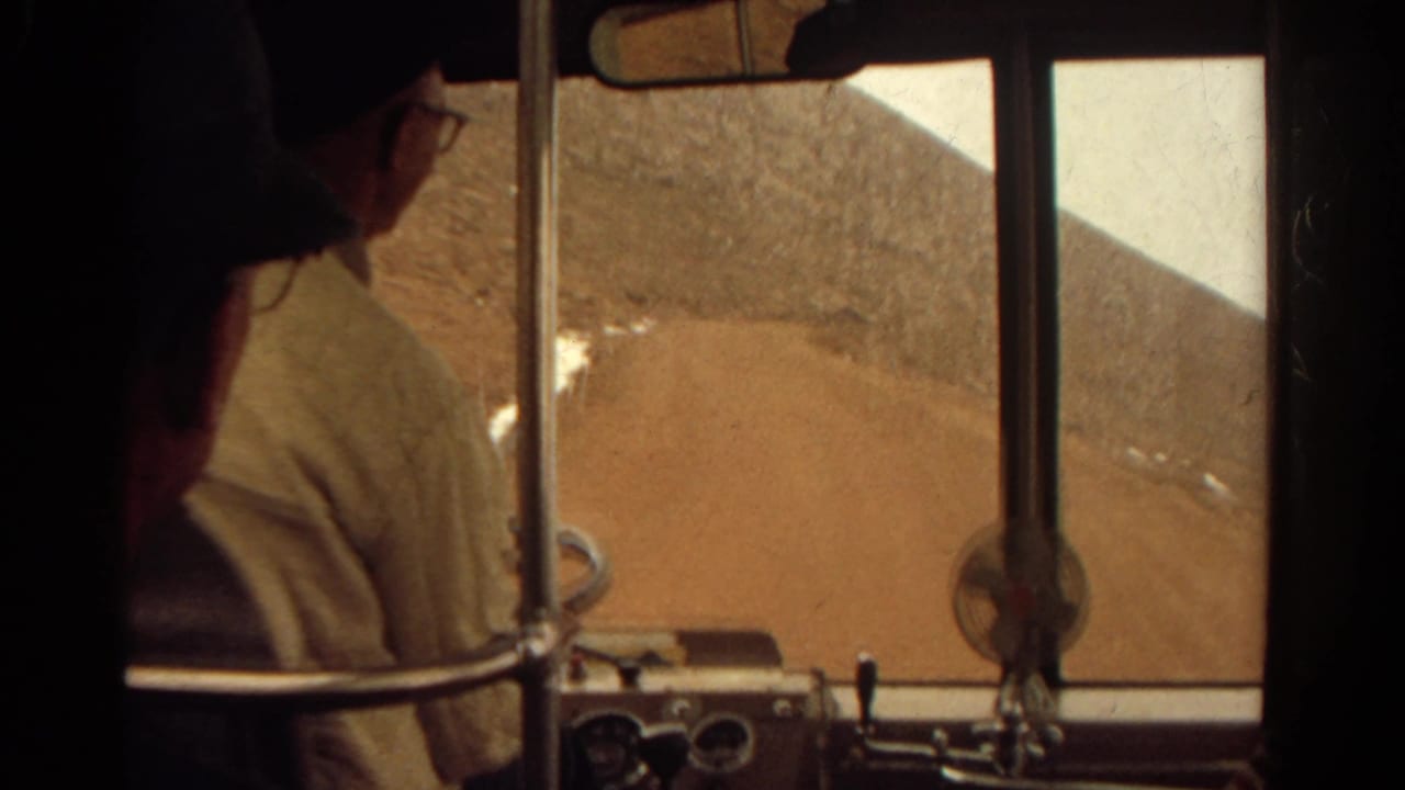 1967 Colorado home-movie frame showing a driver in glasses at the wheel on a rugged dirt road through dry hills.