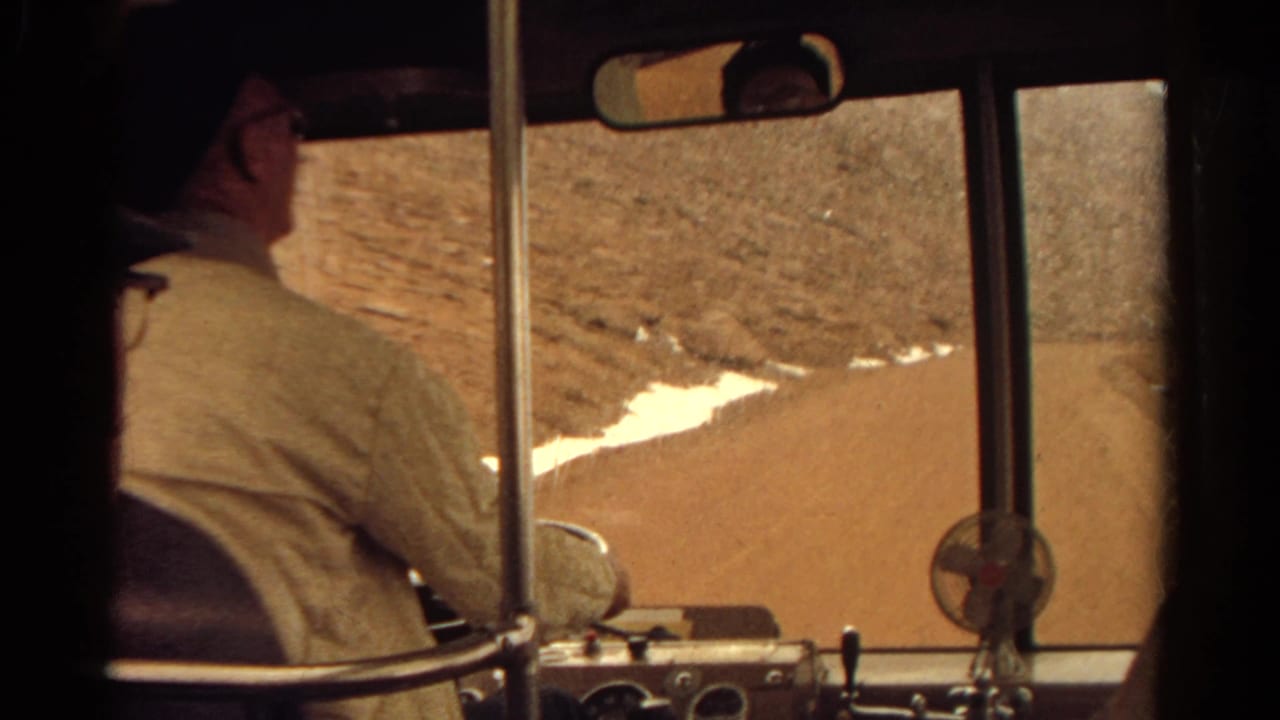 1967 Colorado 8mm frame from inside a bus, showing the driver, dashboard, windshield, and arid hillside with patches of snow.
