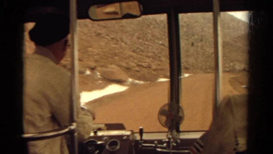 1967 Colorado home-movie view from behind the bus driver, with cabin fixtures, gauges, and a dry hillside road visible ahead.