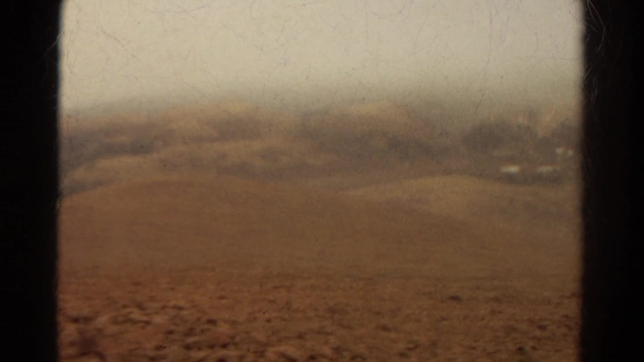 Soft-focus brown hills seen through a vehicle window with dark vertical frame edges.