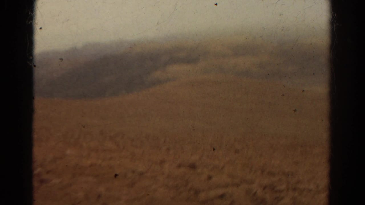 Blurred arid hillside and distant ridge viewed through a dark window frame.