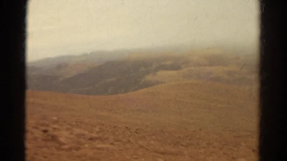 1967 Colorado travel footage showing dusty hills and distant mountains through a vehicle window in faded 8mm color.