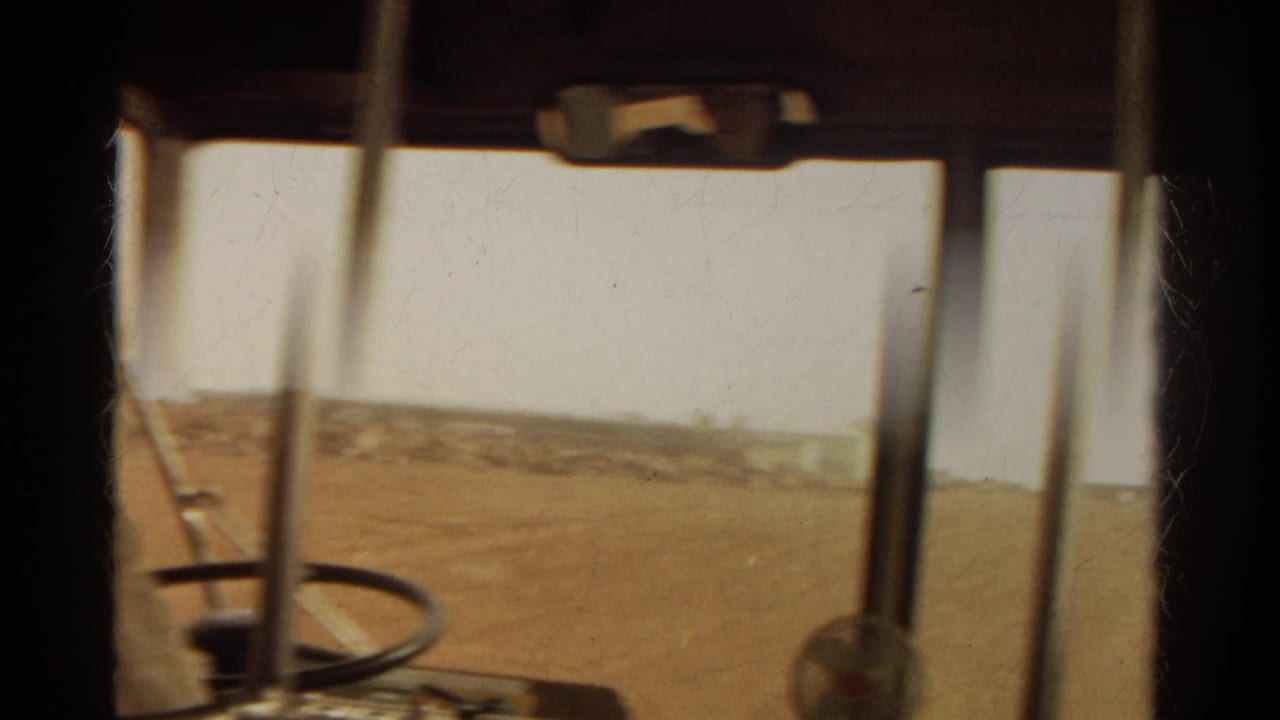 1967 Colorado road-trip footage from inside a vehicle, with window posts, mirror, steering wheel, and dry terrain ahead.