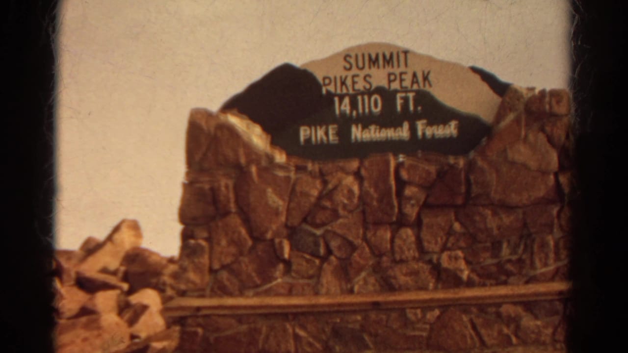 1967 Colorado 8mm frame of the Pikes Peak summit sign set into a stone monument under a bright sky.