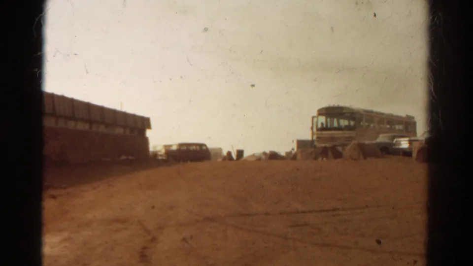 Wide 1967 Colorado summit parking view with a 1960s-style bus, parked cars, rocks, and a dusty lot.