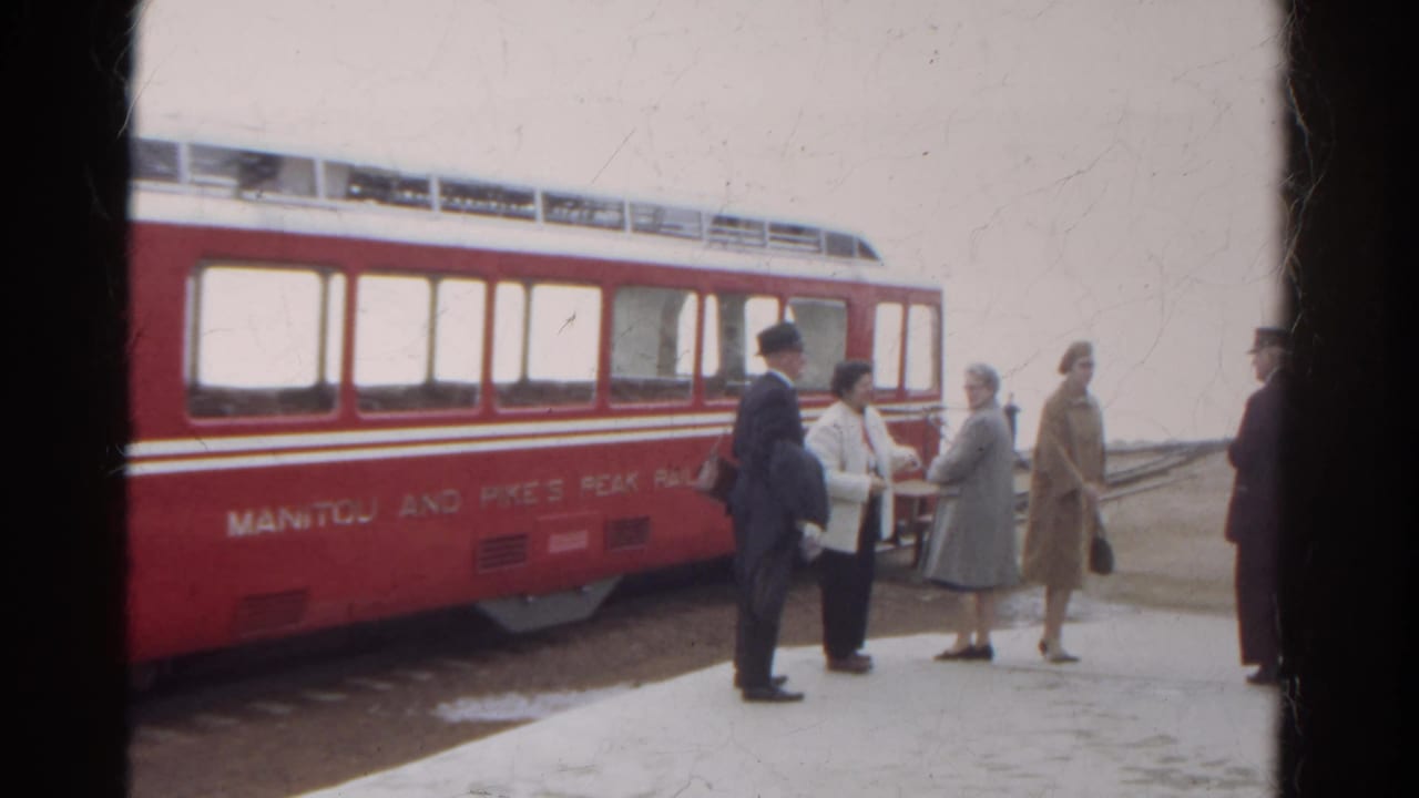 1967 Colorado home-movie frame showing adults in winter clothing beside a red Manitou and Pike's Peak Railway car.