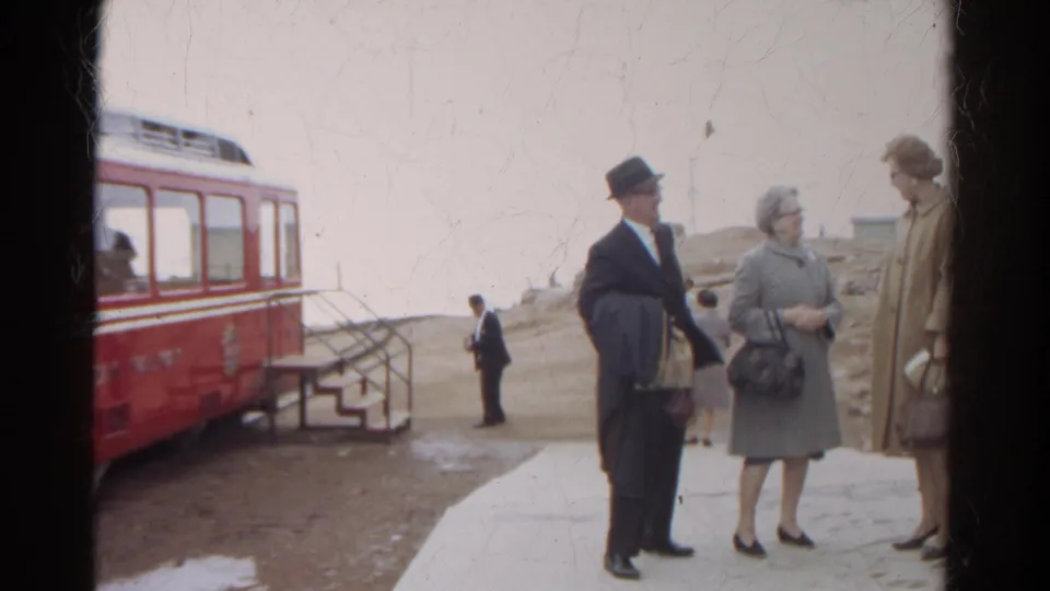 Adults in mid-century coats stand and converse near a red Manitou and Pike's Peak Railway car in Colorado.