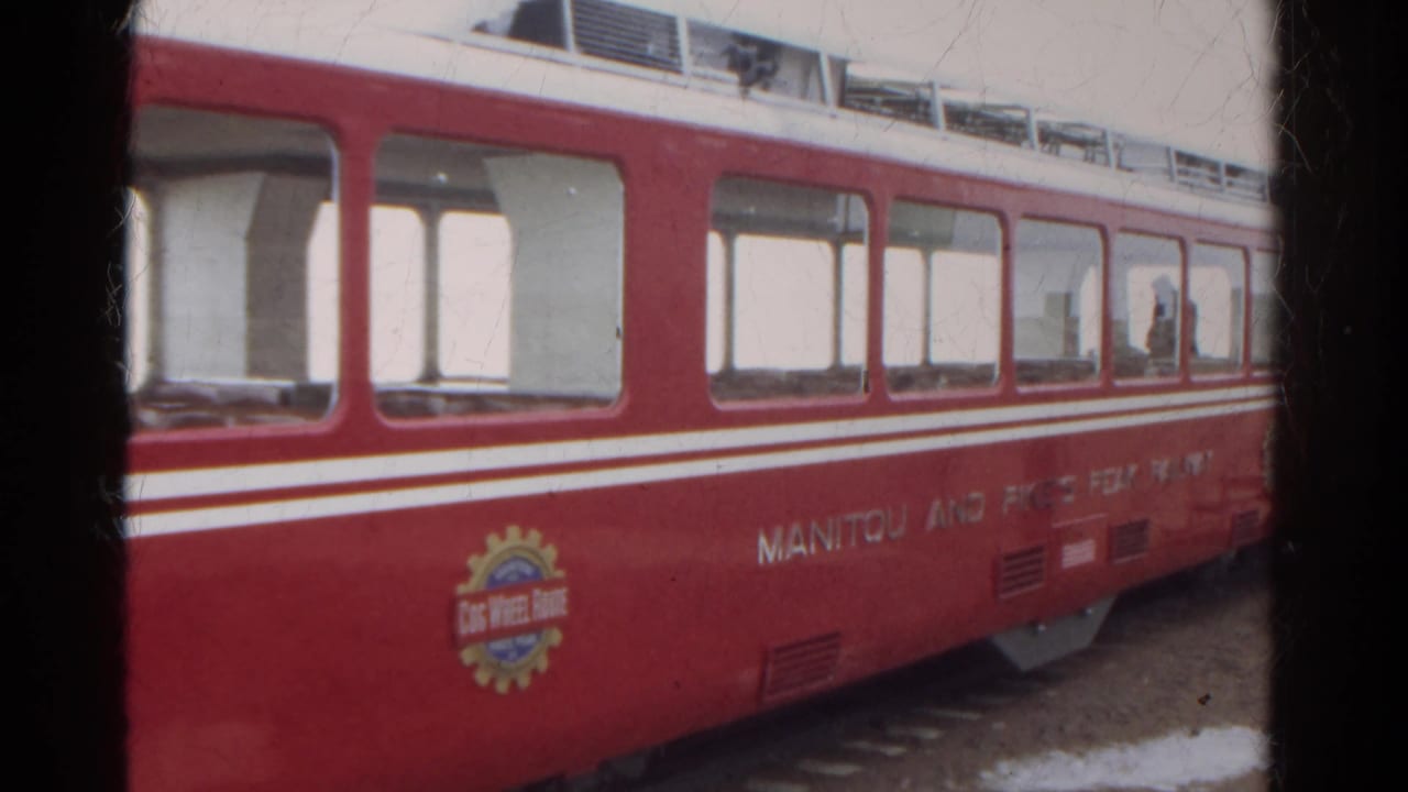 Close side view of a red railway car with windows, logo, and white stripes.