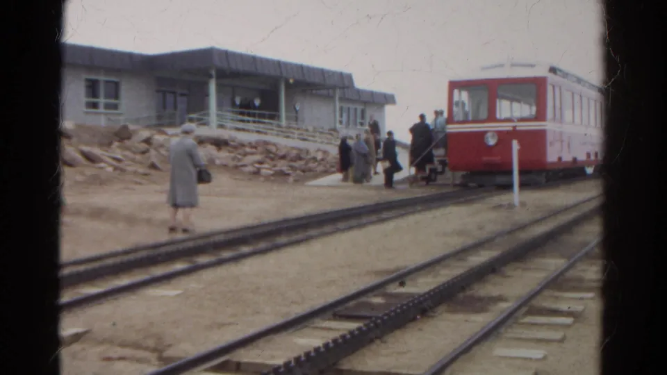 1967 Colorado 8mm frame showing a red railcar by a small station, people gathering, and a woman standing near multiple tracks.