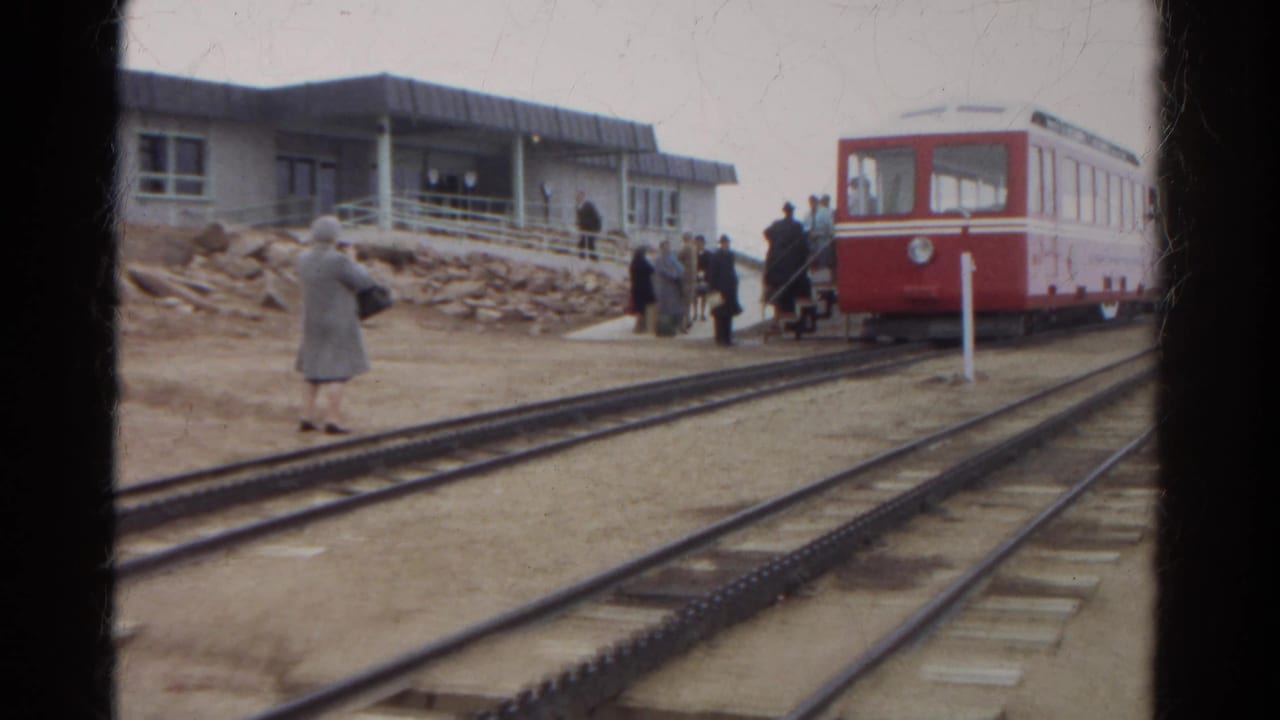 1967 Colorado 8mm frame with a red railcar at the platform, several passengers nearby, and rails leading through the foreground.