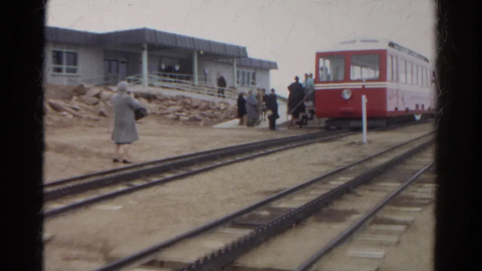 1967 Colorado 8mm frame with a red railcar at the platform, several passengers nearby, and rails leading through the foreground.