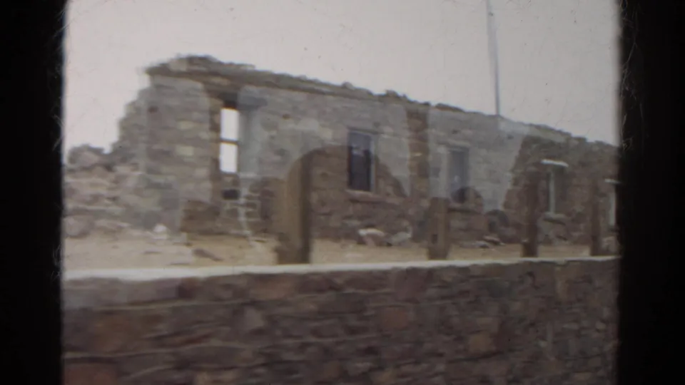 1967 Colorado 8mm frame showing weathered stone ruins, partial wall openings, rubble, and a low foreground wall.