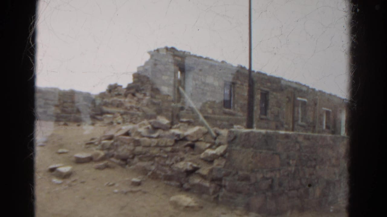 Weathered stone ruin with crumbling walls and rocks on dry ground.