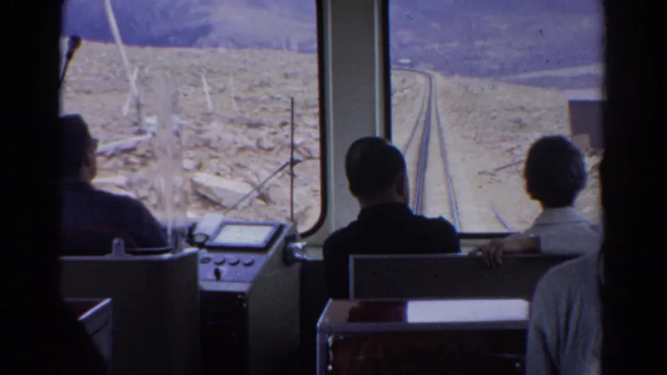 1967 Colorado 8mm frame showing train passengers viewed from behind as the track curves through dry mountain terrain.