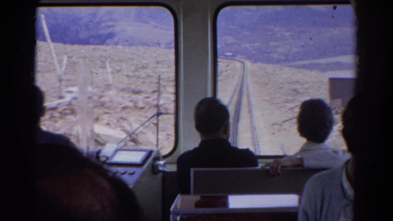 Interior passenger view from a 1967 Colorado train, with travelers facing the windows and mountain tracks ahead.