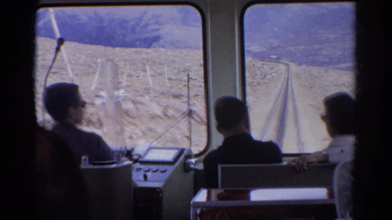 1967 Colorado 8mm footage showing passengers inside a mountain railway car facing tracks and arid slopes ahead.
