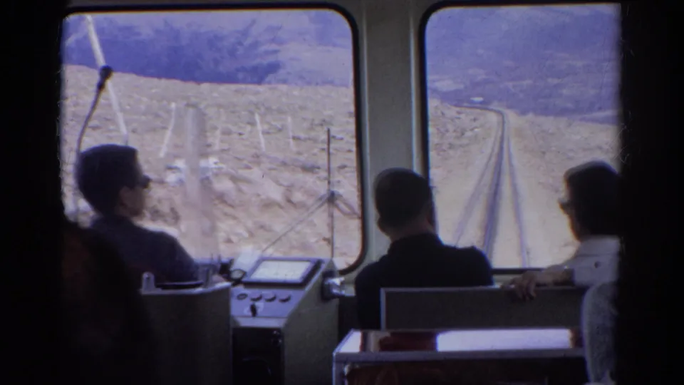 1967 Colorado 8mm footage showing passengers inside a mountain railway car facing tracks and arid slopes ahead.