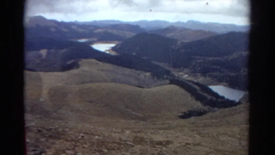 Scenic Colorado mountain view from 1967 8mm footage, showing hills, lakes, forested areas, and distant ridges.