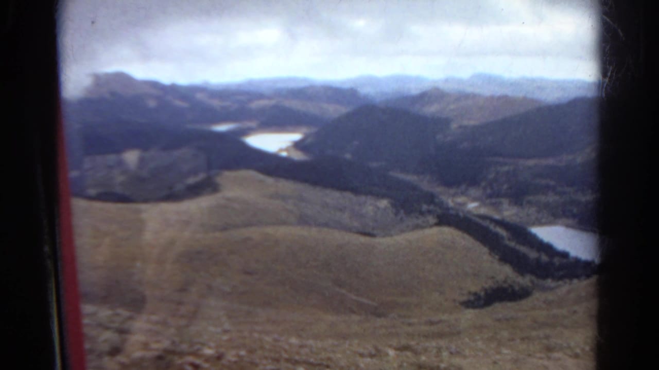 Forested foothills and pale water seen through a vehicle window.