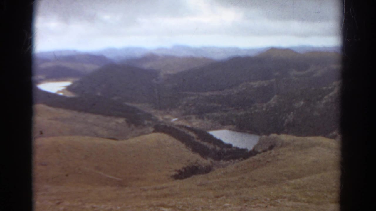 1967 Colorado 8mm aerial view from a plane over ridges, valleys, dark forest bands, and scattered alpine lakes.