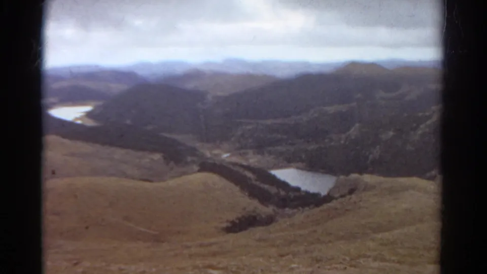 1967 Colorado 8mm aerial view from a plane over ridges, valleys, dark forest bands, and scattered alpine lakes.