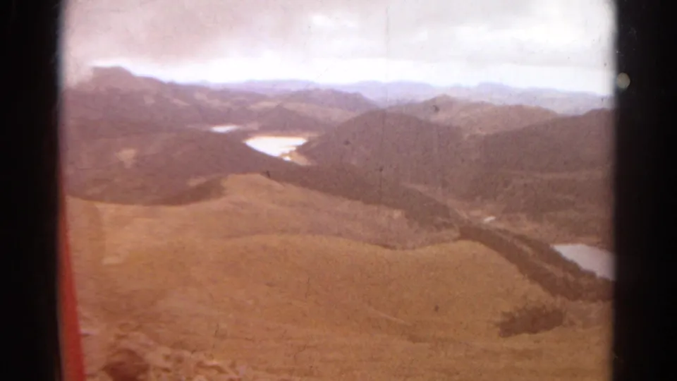 Faded 1967 Colorado 8mm aerial frame with brown hills, distant mountain layers, lakes, and visible gate shadows.