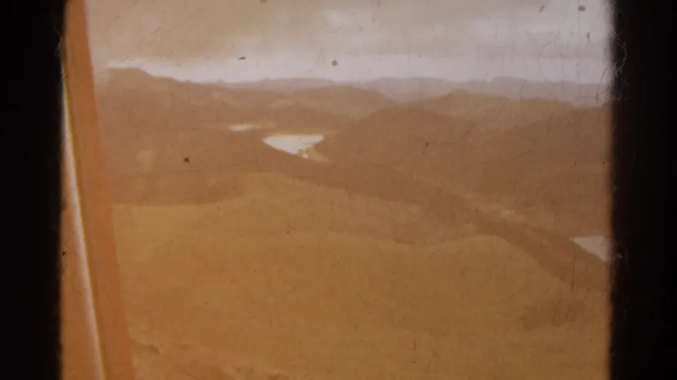 1967 Colorado aerial frame with strong color fade, a plane-window edge, open mountain slopes, distant ridges, and small lakes.