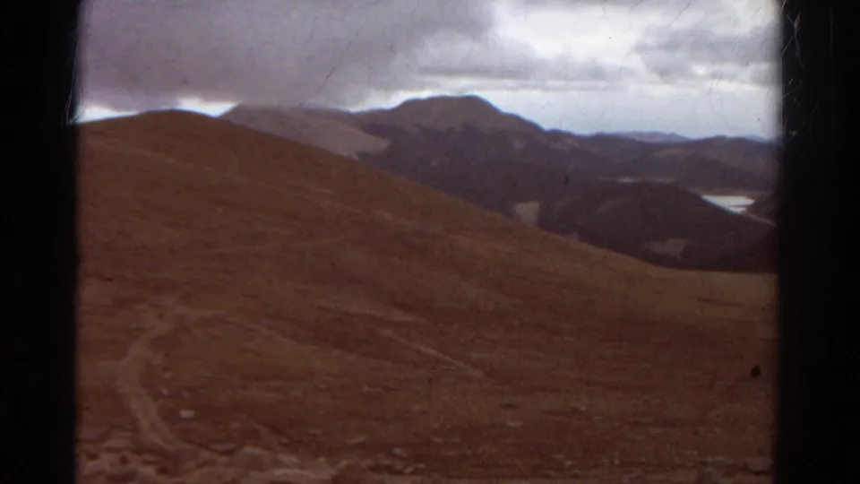 A wider Colorado hillside view from 1967 8mm footage shows rolling terrain, distant ridges, and a lake tucked in the valley.