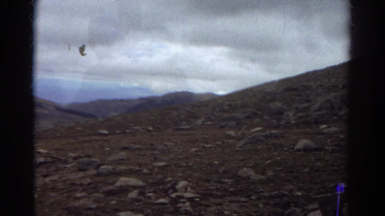 Stony mountain slope and distant ridges under a gray overcast sky.