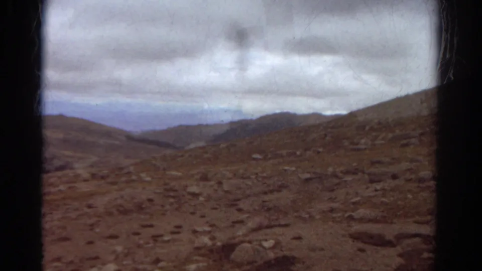 1967 Colorado home-movie view across a rocky hillside toward distant mountains and a clouded horizon.