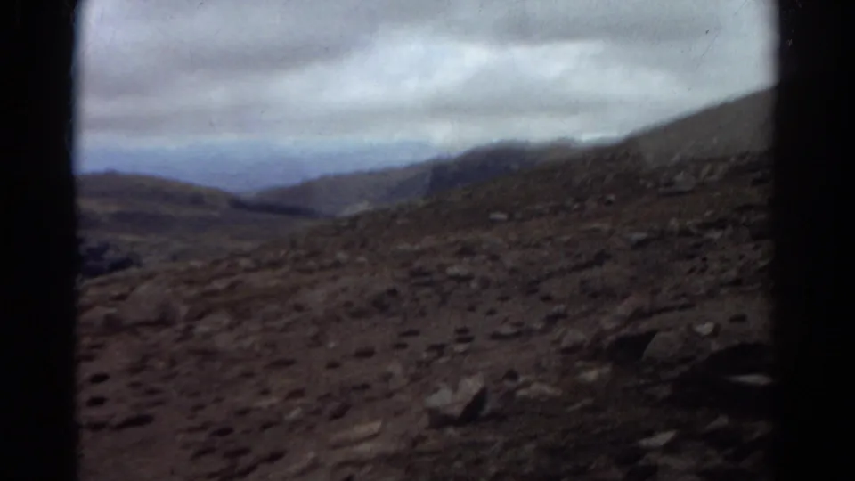 Colorado 8mm travel footage frame with rocky terrain, soft focus, distant slopes, and heavy cloud cover.