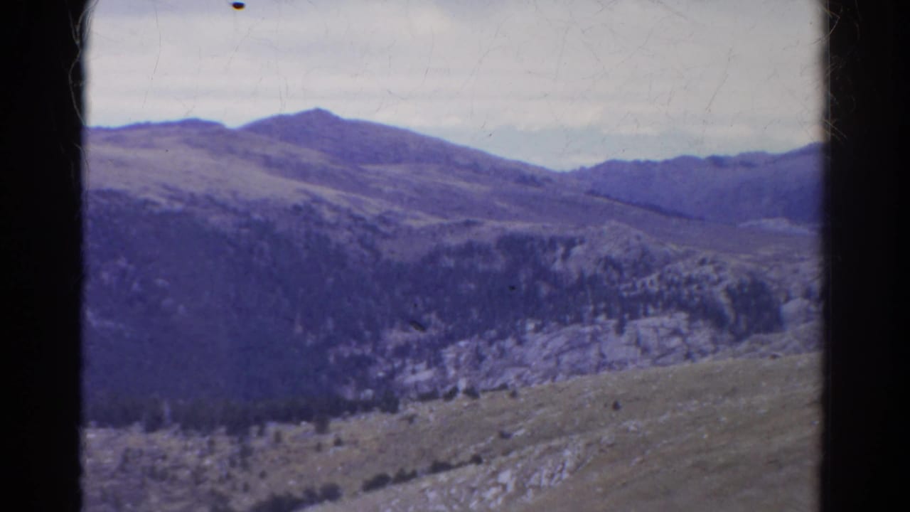 Distant mountain ridges and forested slopes under a cloudy sky, framed by dark film gate edges.